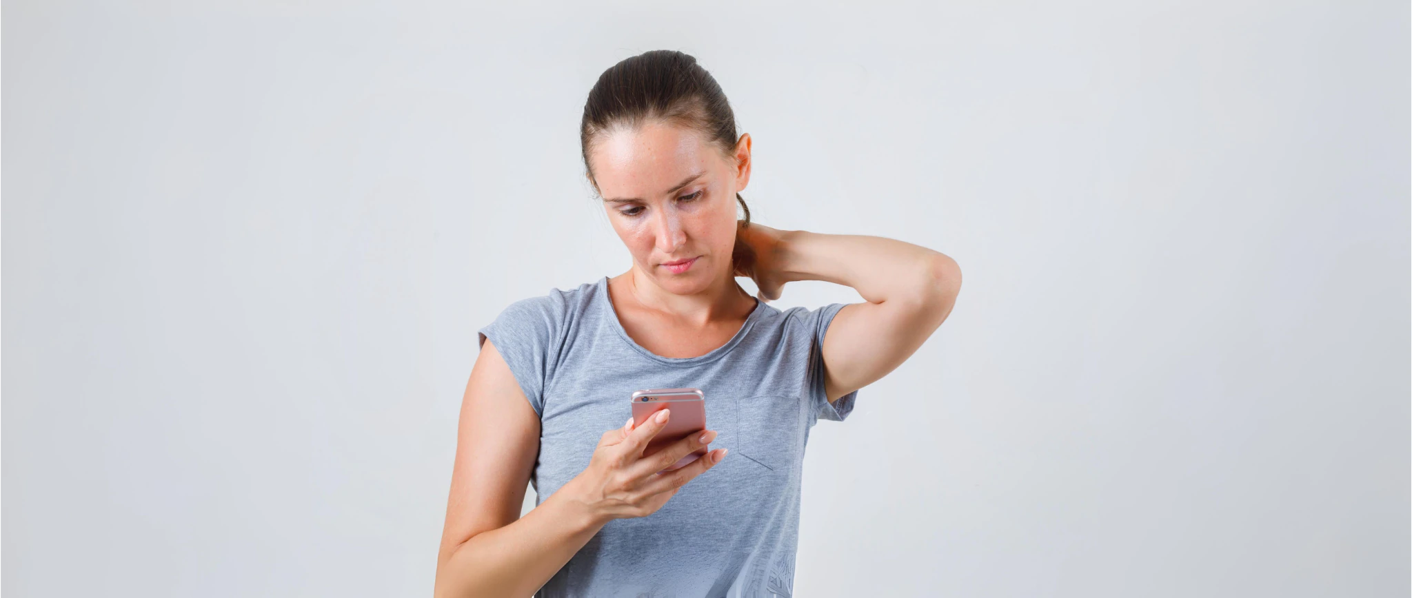 The woman looks at the phone with her head forward and rubs her neck.