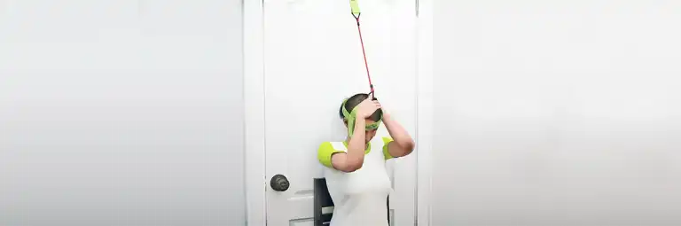 Woman performing the back-of-neck stretch, one of the best stiff neck stretches for pain relief, using the Bejoyland NECKY adjustable neck trainer.