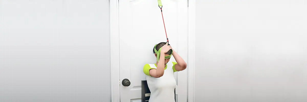 Woman performing the back-of-neck stretch, one of the best stiff neck stretches for pain relief, using the Bejoyland NECKY adjustable neck trainer.